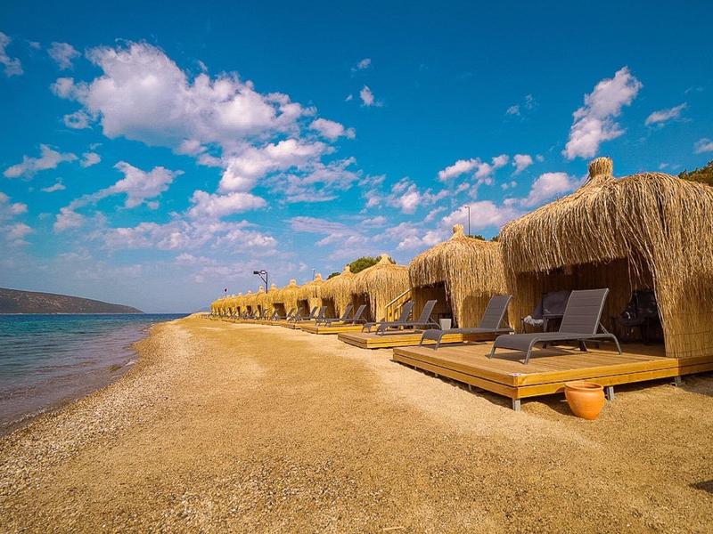 Large plage de sable avec chaises longues en paille et ciel bleu acier