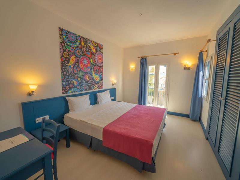 Chambre d'hôtel lumineuse avec lit double, meubles bleus et œuvre murale colorée.