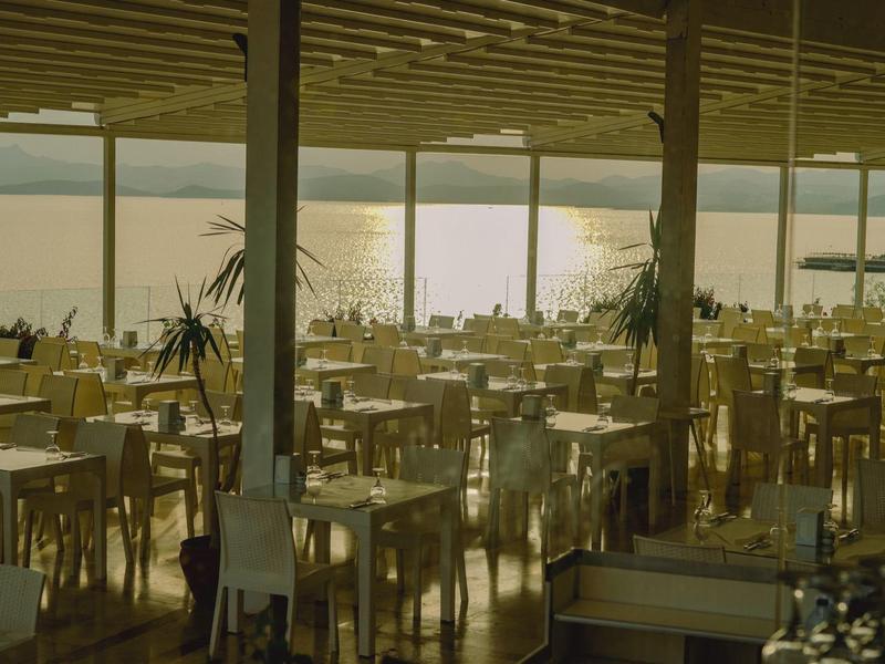 Terrasse d'hôtel ensoleillée avec de nombreuses tables et chaises donnant sur la mer.