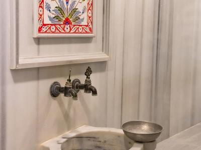 Mała wisząca marmurowa umywalka z ozdobnym kranem i metalową miską obok.