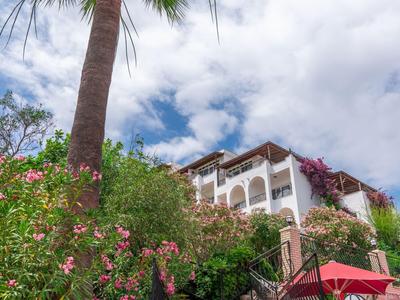 Treppenaufgang zu einem Hotel mit mediterraner Bepflanzung und Palmen unter blauem Himmel.
