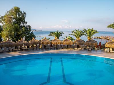 Pool mit Liegestühlen und Palmen mit Meerblick an einem sonnigen Tag.