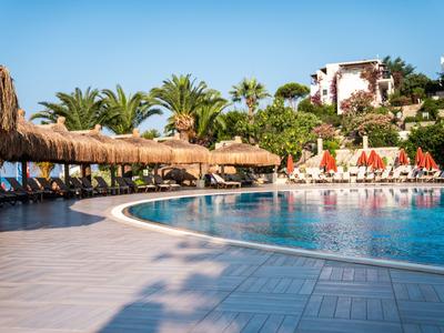 Großer, geschwungener Hotelpool mit Sonnenliegen und Palmen bei klarem Himmel.