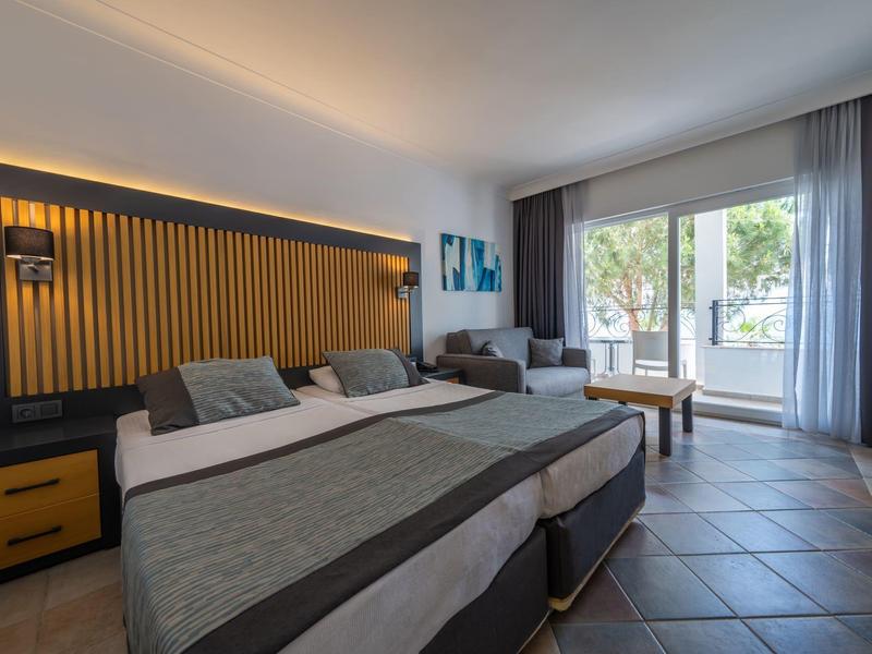 Nowoczesny pokój hotelowy z podwójnym łóżkiem, przytulnym miejscem do siedzenia i balkonem z widokiem na drzewa.