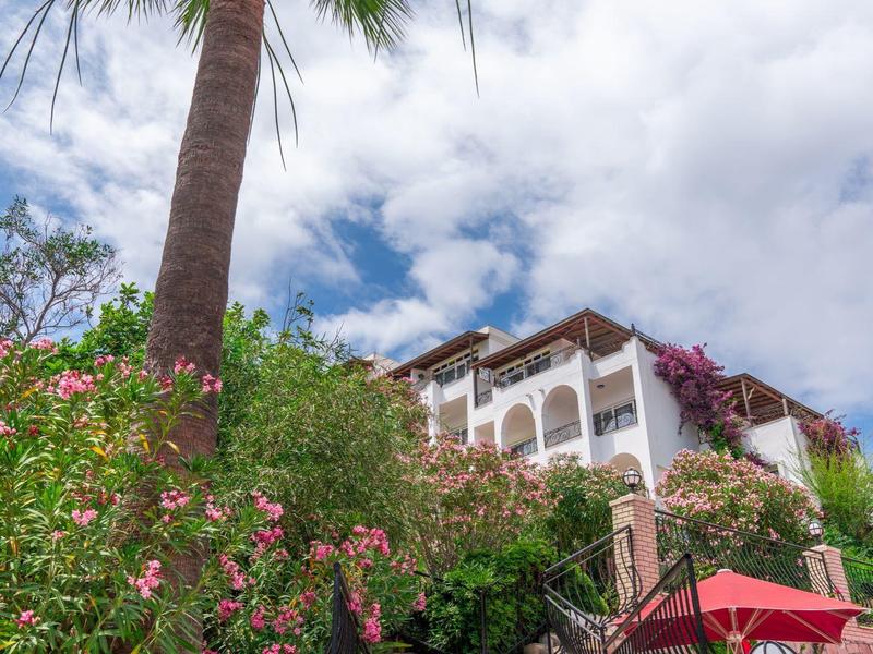 Schody prowadzą do hotelu z balkonami, otoczonego palmami i kwitnącymi krzakami.