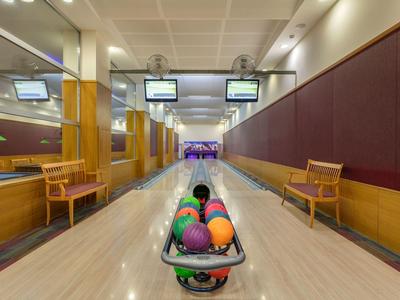 Blick auf eine Bowlingbahn mit bunten Kugeln in der Kugelablage und zwei Holzbänken an der Seite.