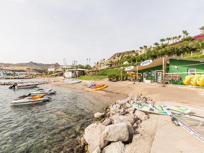 Küste mit Strand, Wasserfahrzeugen und Hotels auf Hügeln bei bewölktem Himmel.