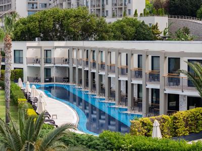 Moderner Hotelkomplex mit rechteckigem Pool und grüner Umgebung in urbaner Lage.