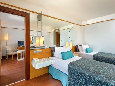 Modernes Hotelzimmer mit zwei Einzelbetten, Holzboden und angrenzendem Wohnzimmer.