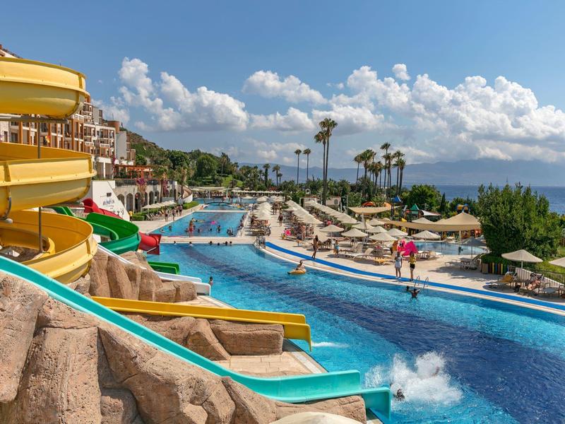 Park wodny z zjeżdżalniami, basenem i leżakami w słonecznym kurorcie plażowym.