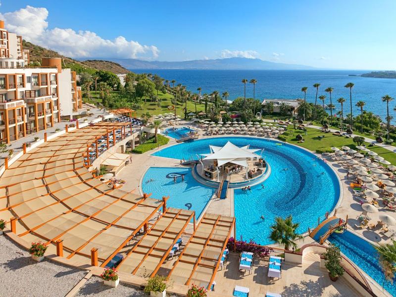 Hotel z dużym okrągłym basenem, leżakami i widokiem na morze pod niebieskim niebem