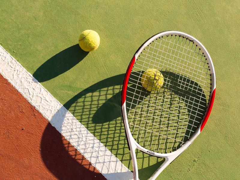 Rakieta tenisowa i piłka na korcie z cieniami.