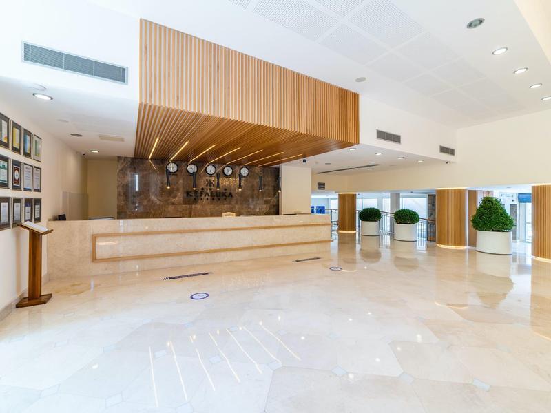 Jasne lobby hotelowe z recepcją, nowoczesnym drewnianym sufitem i polerowaną marmurową podłogą.