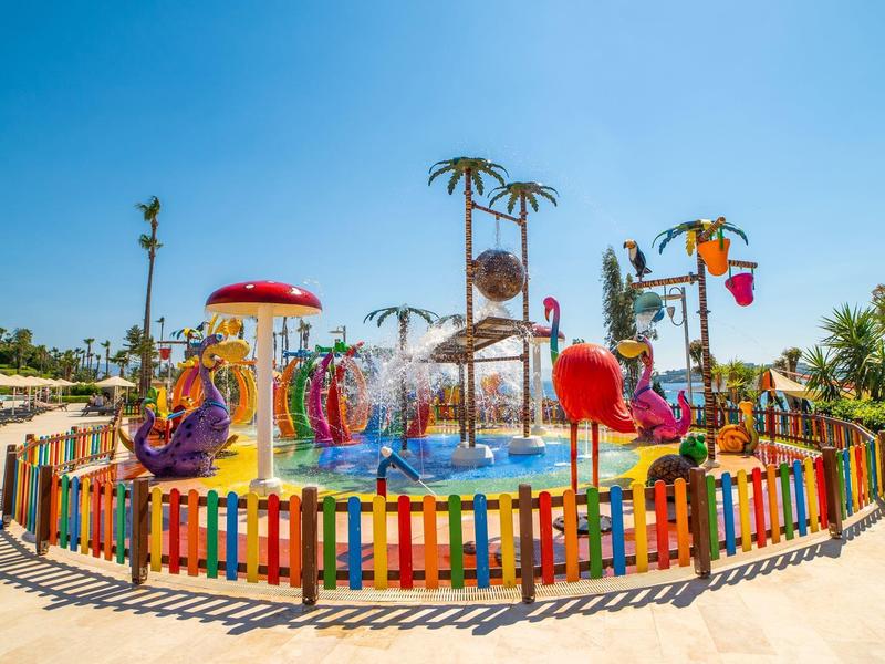 Kolorowy plac zabaw wodny z figurkami i palmami w słonecznym otoczeniu hotelowym.