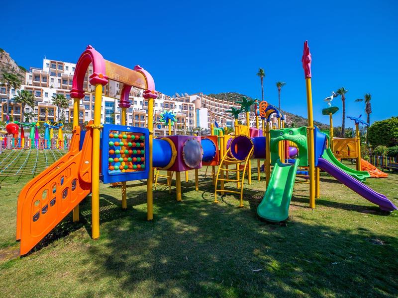 Kolorowy plac zabaw z zjeżdżalniami i konstrukcją do wspinaczki przed ośrodkiem wypoczynkowym i górami.