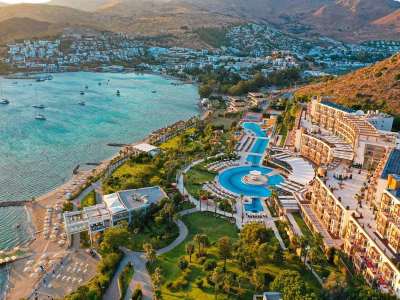 Widok z lotu ptaka ośrodka z basenami i plażą u podnóża wzgórza.