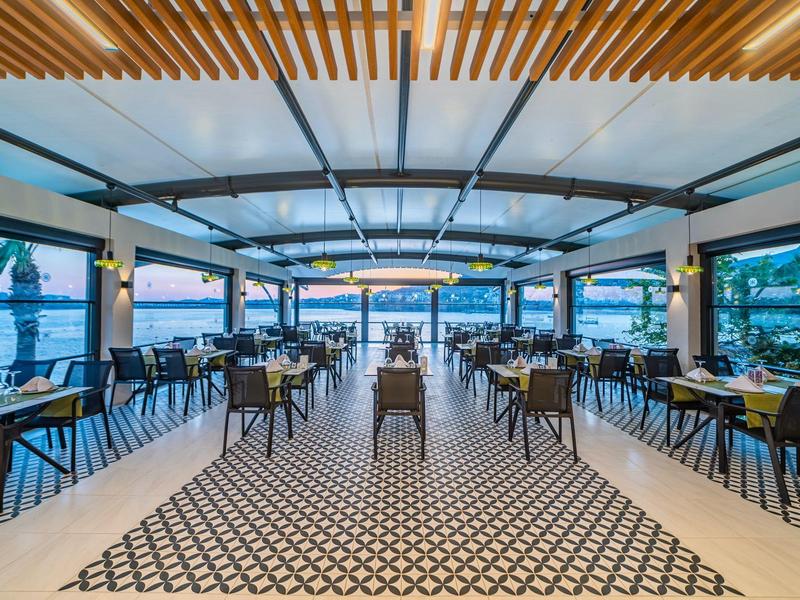 Przestronna otwarta restauracja z nowoczesnymi meblami i widokiem na wodę i palmy.