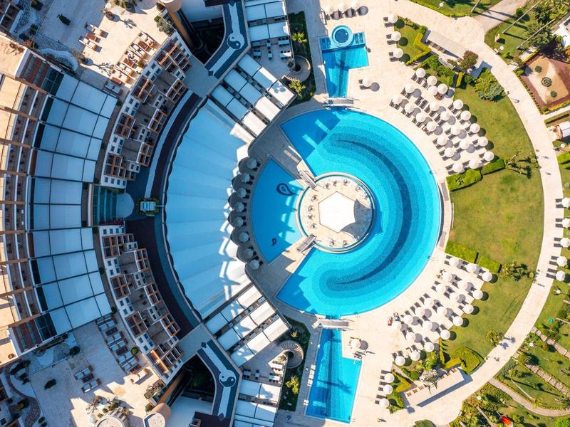 Widok z lotu ptaka na hotel z okrągłym basenem i leżakami na zewnątrz.