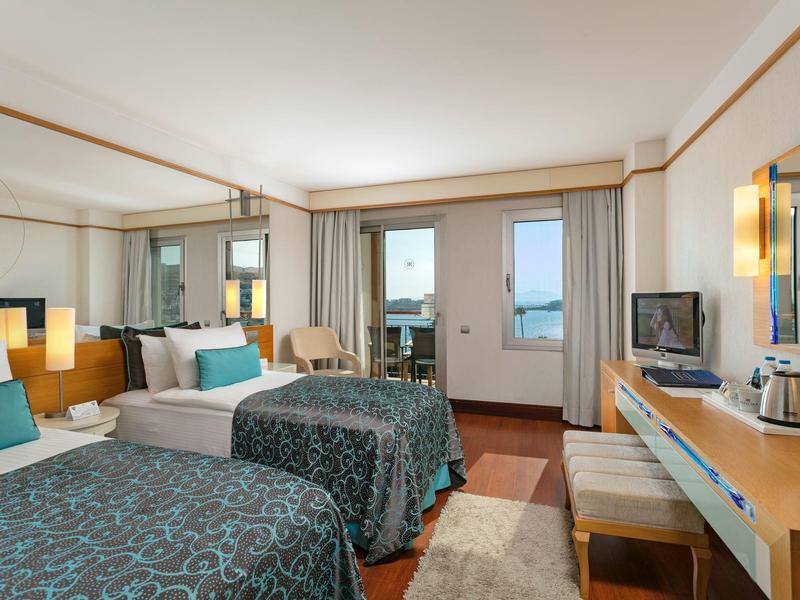Pokój hotelowy z dwoma łóżkami, biurkiem, krzesłami i balkonem z widokiem na morze.