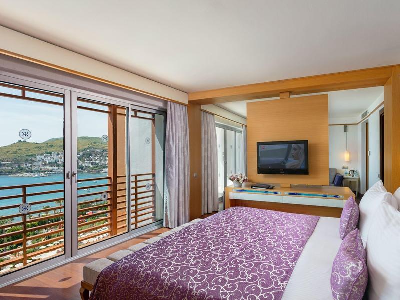 Pokój hotelowy z dużym łóżkiem i widokiem na morze przez okna od podłogi do sufitu.