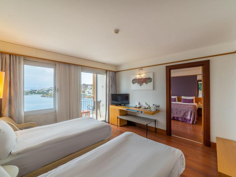 Jasny pokój hotelowy z dwoma pojedynczymi łóżkami, okno z widokiem na wodę i balkon.