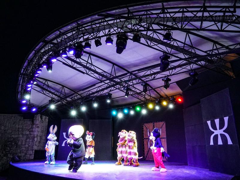 Scena z kolorowymi światłami i przebranymi postaciami nocą w hotelowej sali widowiskowej.