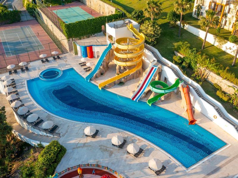 Basen rekreacyjny z zjeżdżalniami wodnymi i parasolami w kompleksie hotelowym w świetle dziennym.