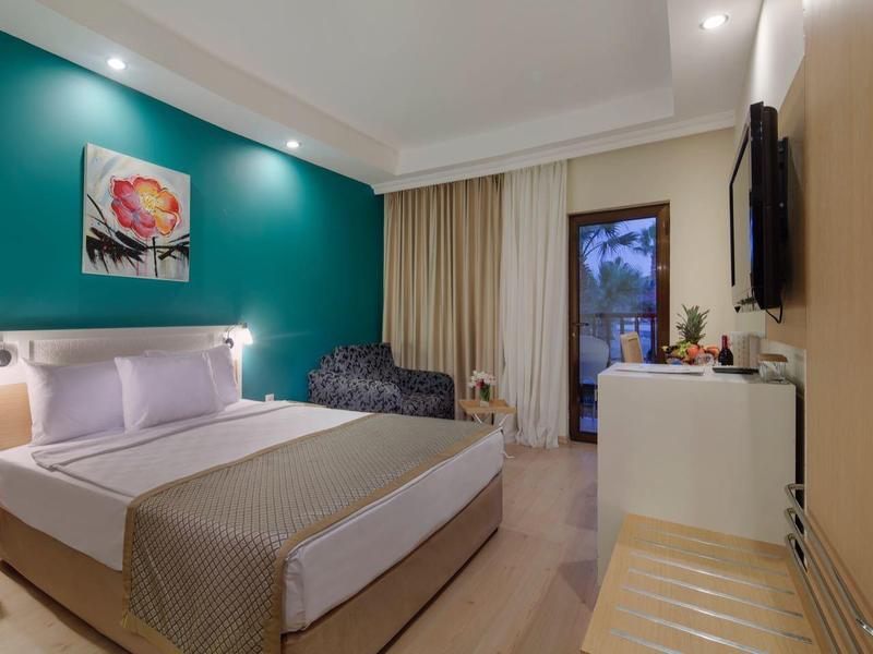 Moderne hotelkamer met groot bed, teal accentmuur en raam met gordijnen.