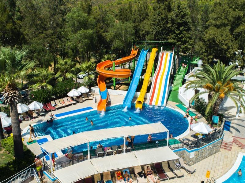 Kleurrijke waterglijbanen en zwembad omgeven door bomen en ligstoelen bij een vakantieoord.