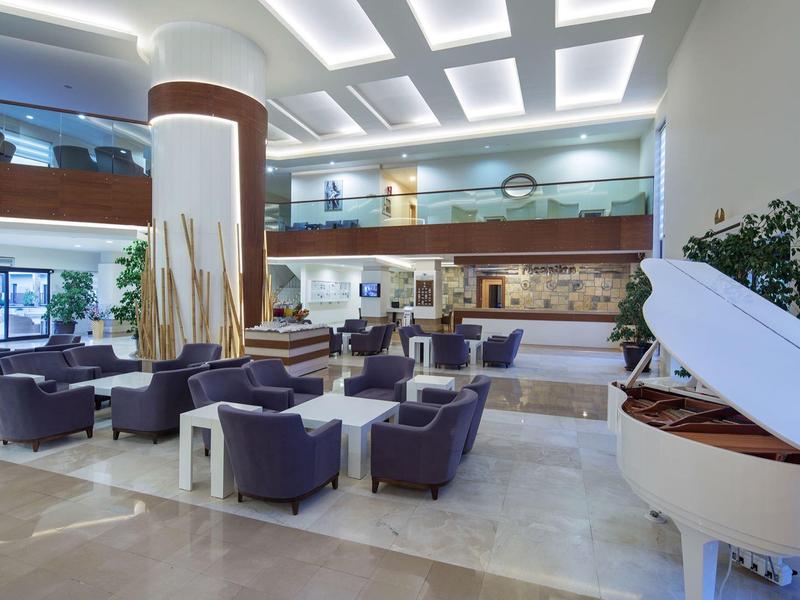 Ruime hotel lobby met moderne zitplaatsen, een witte vleugel en een mezzanine die uitkijkt op de ruimte.