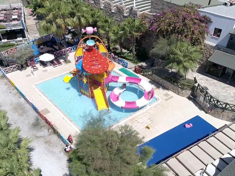 Kleurrijke waterspeeltuin met glijbanen en zwembaden, omringd door palmbomen en gebouwen.