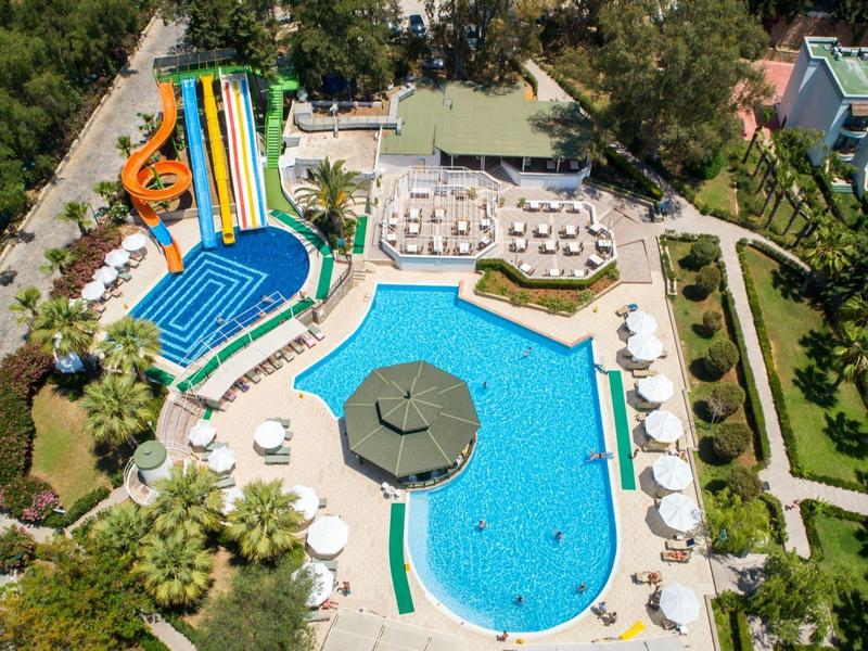 Luchtfoto van een hotelzwembad met glijbanen, parasols, ligstoelen en groen rondom.