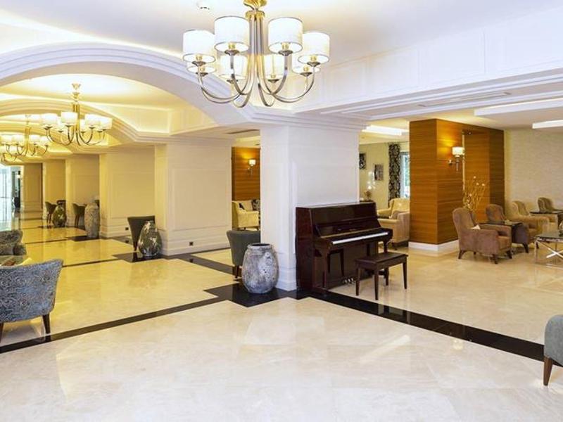 Grote hotel-lobby met zithoeken, piano en elegante verlichting.