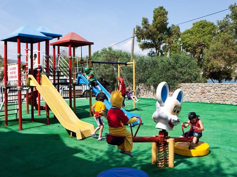 Een kleurrijke kinderspeeltuin met glijbanen en draaimolen bij zonnig weer.