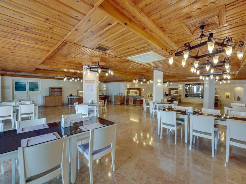 Licht restaurant met houten balkenplafond, witte stoelen en decoratieve verlichting.