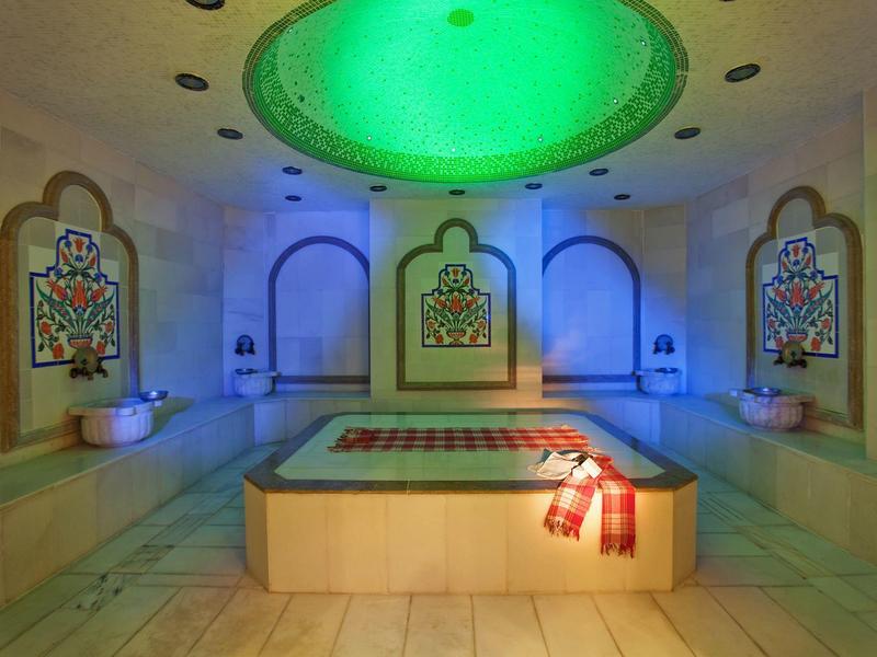 Interieur van een Arabisch geïnspireerd hamam met verlicht plafond en stenen bank.