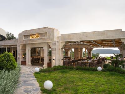 Offener Restaurantbereich mit gedeckten Tischen und Blick auf das Meer bei bewölktem Himmel.