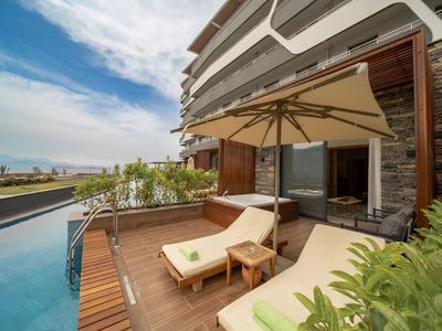 Terrasse mit Liegestühlen und Sonnenschirm neben einem Pool und modernem Hotelgebäude.