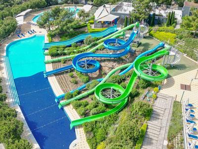 Wasserpark mit großen, bunten Wasserrutschen und Pool am Meer mit Yacht im Hintergrund.