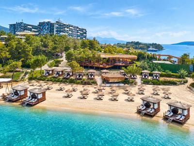 Luxuriöses Strandhotel mit Sonnenliegen, grünen Bäumen und klarem blauen Meer.