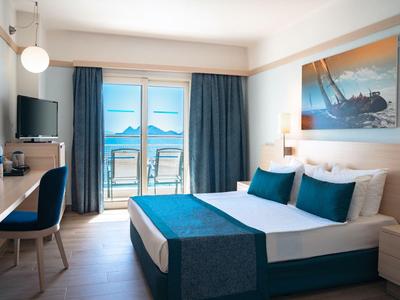 Modern eingerichtetes Hotelzimmer mit Doppelbett und Meerblick durch Balkonfenster.