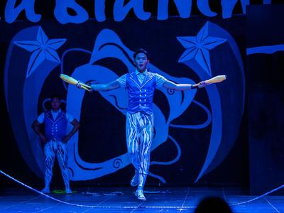 Ein Artist springt mit zwei Keulen in der Hand auf einer Bühne bei einer Zirkusvorstellung.