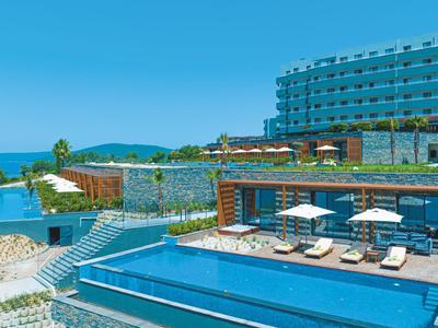 Moderner Hotelkomplex mit Pools und Liegestühlen nahe eines blauen Meeres unter klarem Himmel.