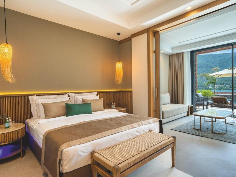 Habitación de hotel moderna con cama grande, zona de estar y vista a la terraza y al mar