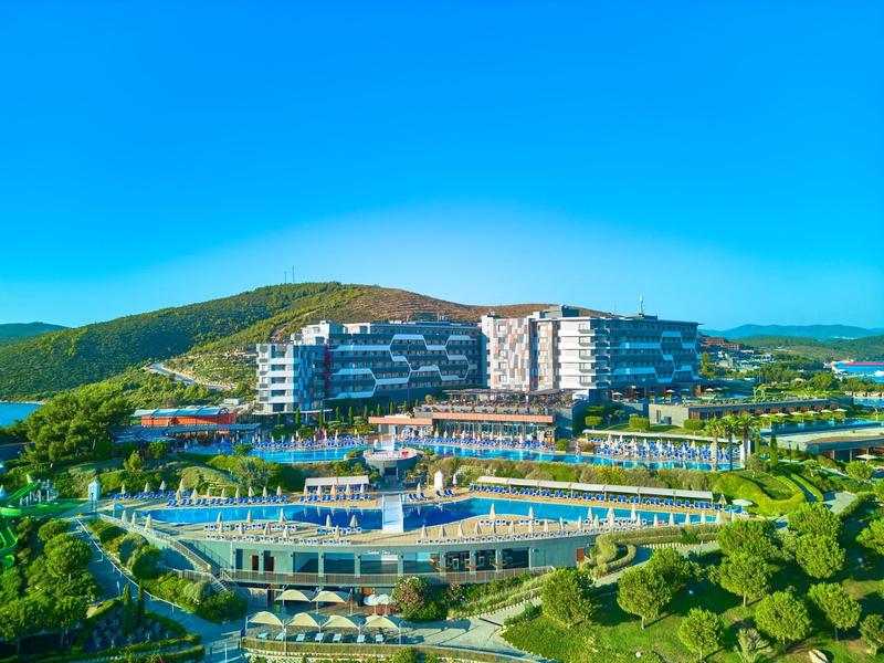 Complejo hotelero moderno en paisaje verde con piscina y montañas al fondo bajo un cielo despejado.
