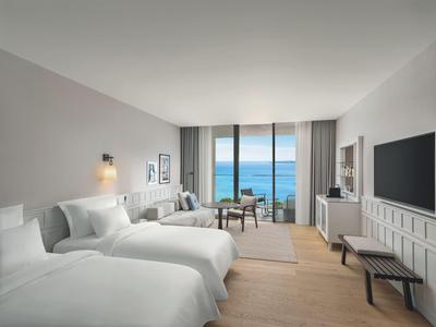 Helles Hotelzimmer mit zwei Betten, Sitzbereich und Meerblick durch große Fenster