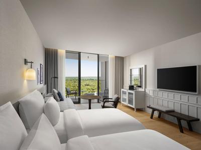 Habitación de hotel moderna con dos camas dobles, ventana grande y vista al verde.