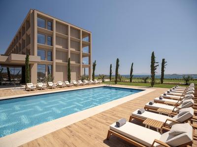 Moderner Hotelpool mit Liegestühlen und klarer blauer Wasserfläche unter klarem Himmel.