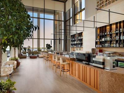 Helles Hotelrestaurant mit langer Bar, Holztresen, Barhockern und großen Fenstern.