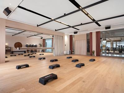 Moderner heller Fitnessraum mit Holzfußboden, Step-Bänken und großen Spiegeln.